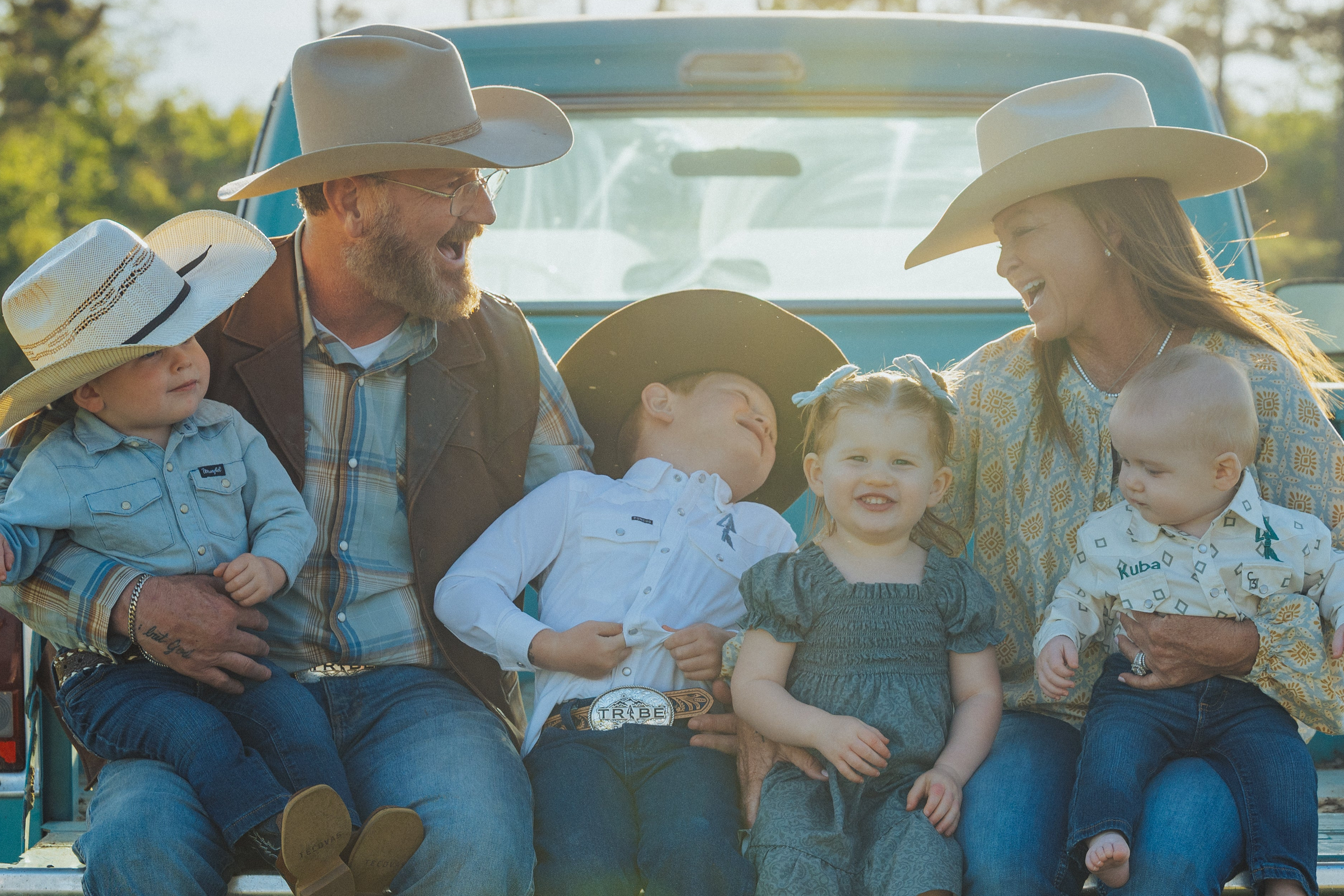 The Tribe Ranch family seated in the pasture with cattle behind them